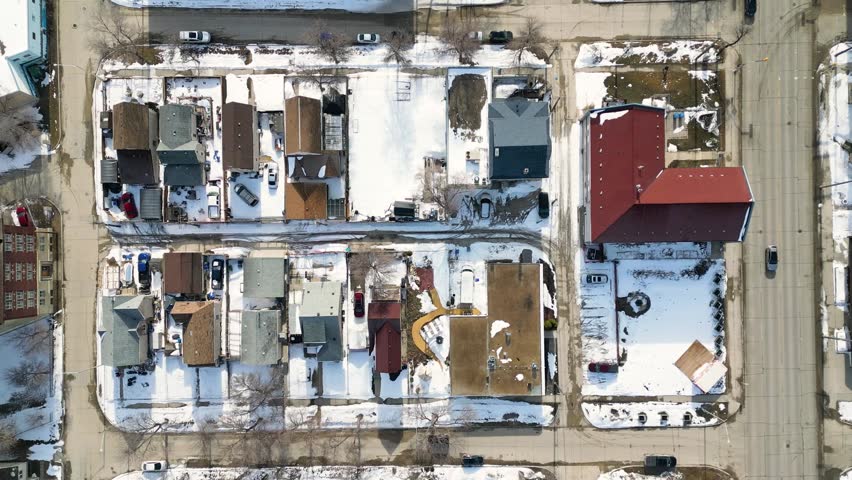 Static top down drone shot of a Winnipeg residential neighborhood with small homes snow covered lawns and light street traffic