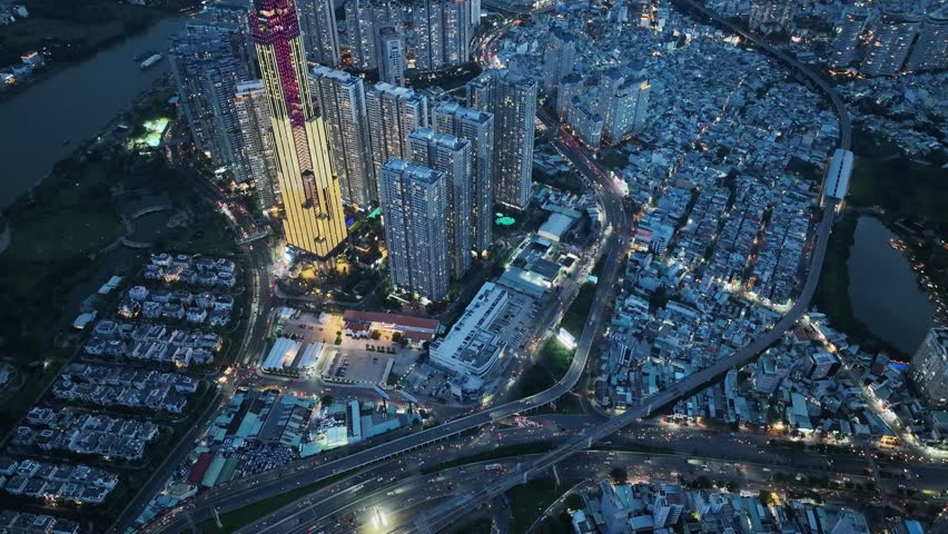 Aerial night view of illuminated skyscraper tower dominating dense residential district with highways and river curves glowing across Ho Chi Minh City.