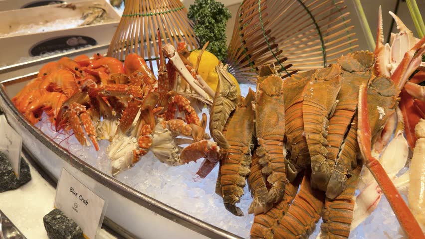 A slow panning shot across a chilled seafood display including crab legs, lobsters, and clams