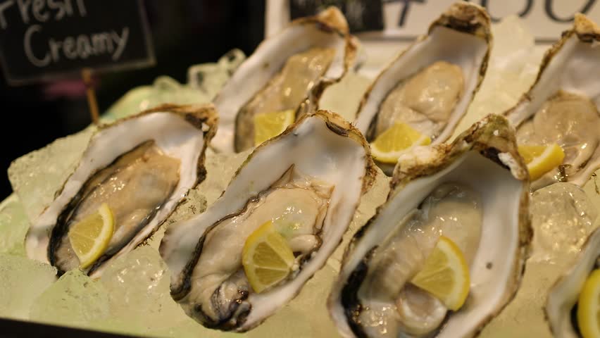 Close-up panning shot of fresh raw oysters served with lemon on ice at Kuromon Market