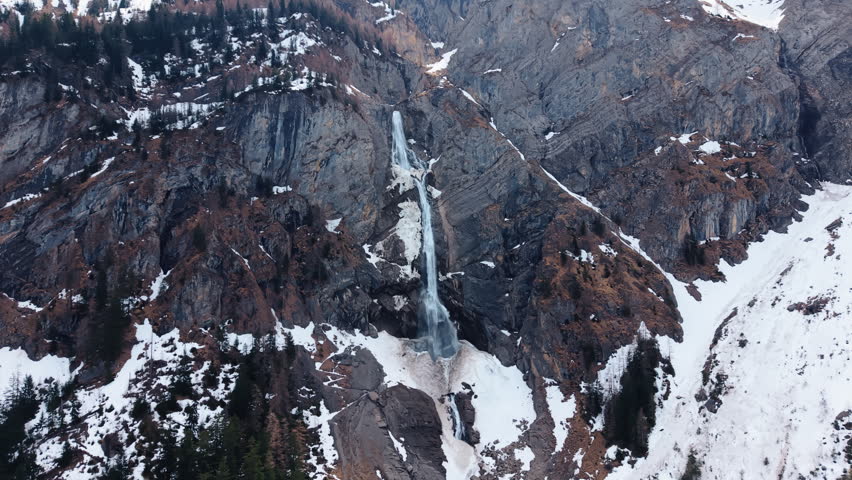 Aerial: Engstligen Falls with snow during the day, second highest fall in Switzerland, orbit drone shot
