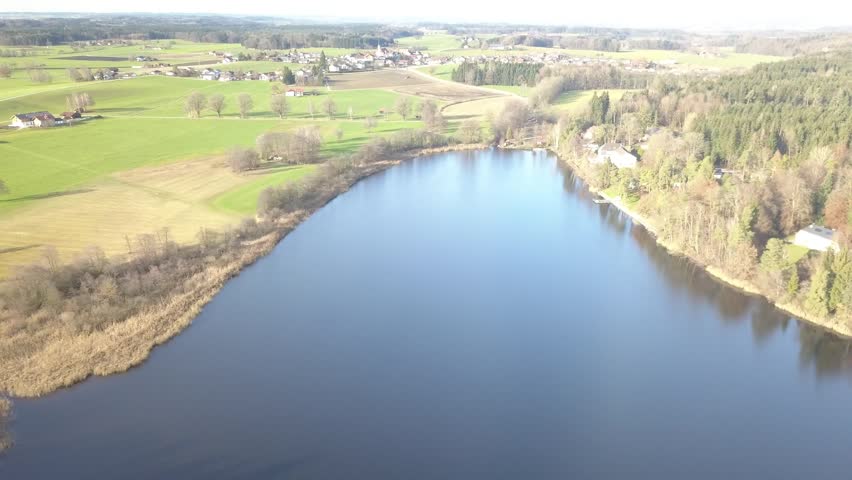Aerial landscape featuring lake, forest and open fields near mountain range in southern Germany.