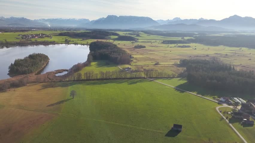 Aerial view of abtsee lake surrounded by fields and forest near mountains in Germany, calm winter landscape with soft light.