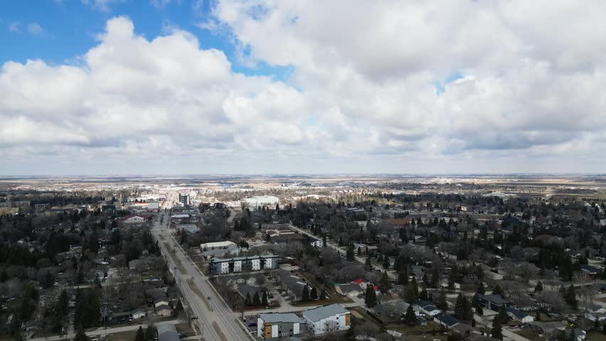 Slow aerial drone shot over a calm small Canadian town with houses trees blue sky and white clouds