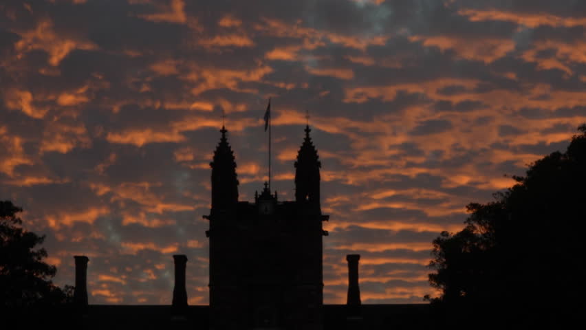 Close up silhouette of historic Gothic university building in Sydney against vivid orange sunset clouds, dramatic sky, real time