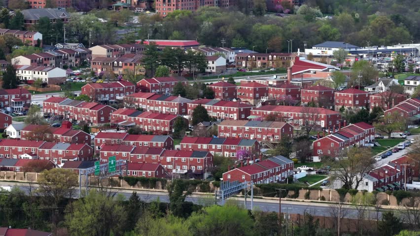 Dense Baltimore neighborhood with rows of red brick townhouses, nearby roadway traffic and urban residential patterns in typical East Coast American city setting. Aerial wide shot. Busy highway road.