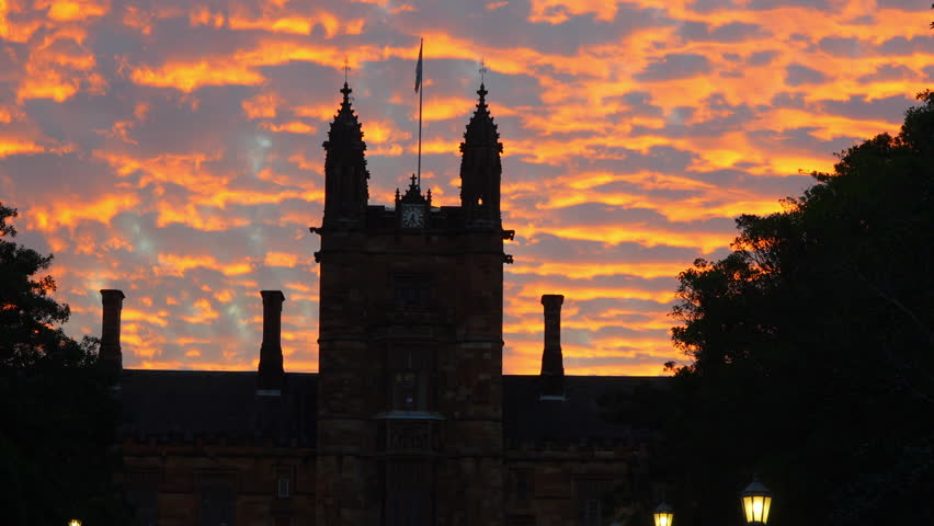 Close up silhouette of historic Gothic university building in Sydney against vivid orange sunset clouds, dramatic sky, real time