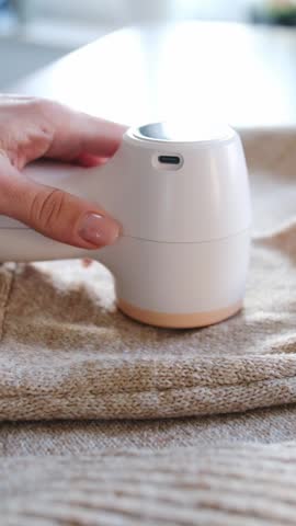 Woman Cleaning A Wool Sweater With An Electric Fabric Shaver On A Table At Home