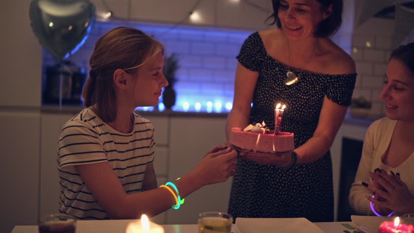 Happy Girl Makes A Birthday Wish And Blows Out The Candles On The Cake Brought By Mom During A Family Birthday Celebration