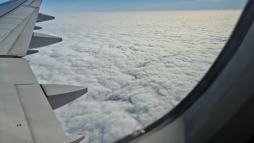 Aerial view from airplane window with wing above soft white clouds. Scenic flight perspective, air travel and aviation concept.