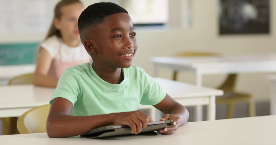 Diverse children learning in class boy with tablet, yellow-shirt boy raising hand after teacher cue. Student, education, technology, school, bright, daylight, windows