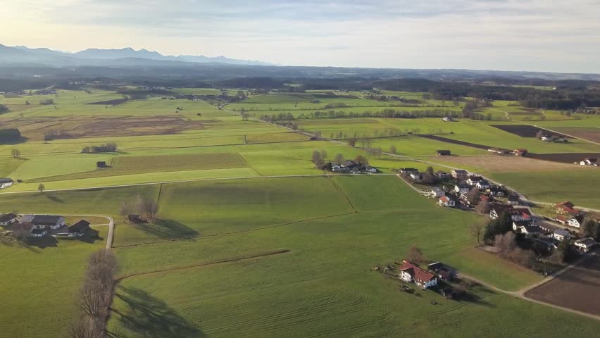 Rural landscape with open fields, scattered homes and mountain range in the distance, calm natural scenery and spacious environment