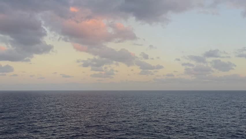 Wide seascape with a low horizon emphasizing a large sky filled with soft, colorful clouds during evening light over open ocean.