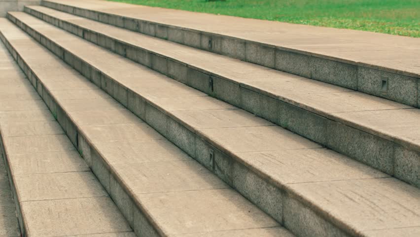 A diagonal architectural shot of wide, outdoor stone steps providing access to a grassy recreational park space.