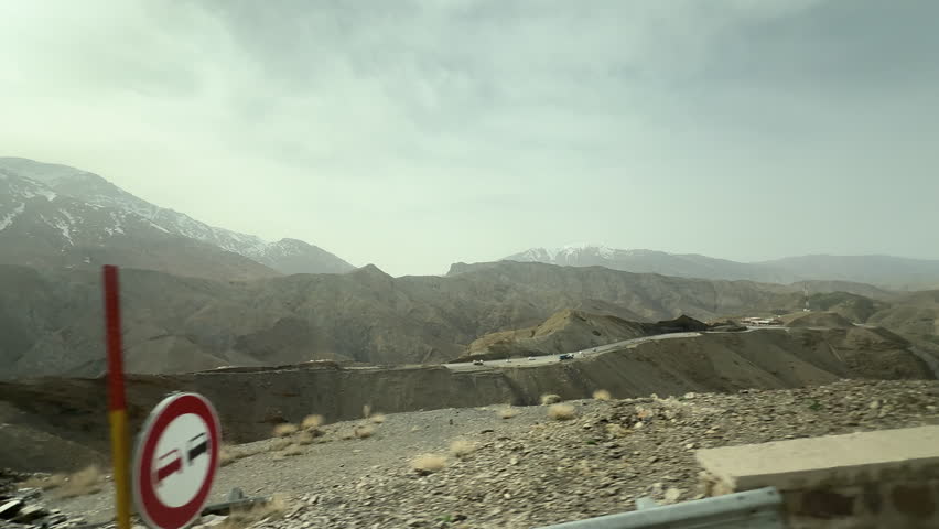 Scenic car ride view of a winding road through a dry, rocky, and snowy mountain landscape at Morocco , tc01