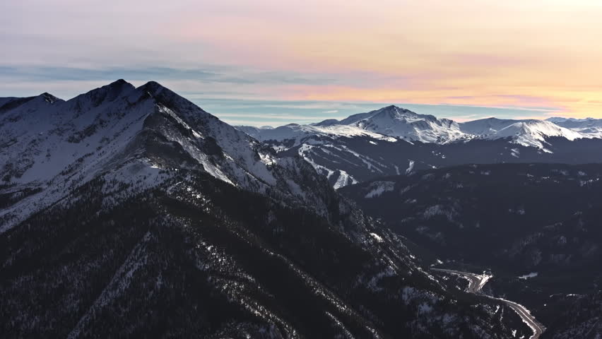 A cinematic, high-flying wide-angle aerial drone shot of snowy peaks surrounding Dillon and Frisco, slowly revealing the ski slopes of Breckenridge Ski Resort in Colorado