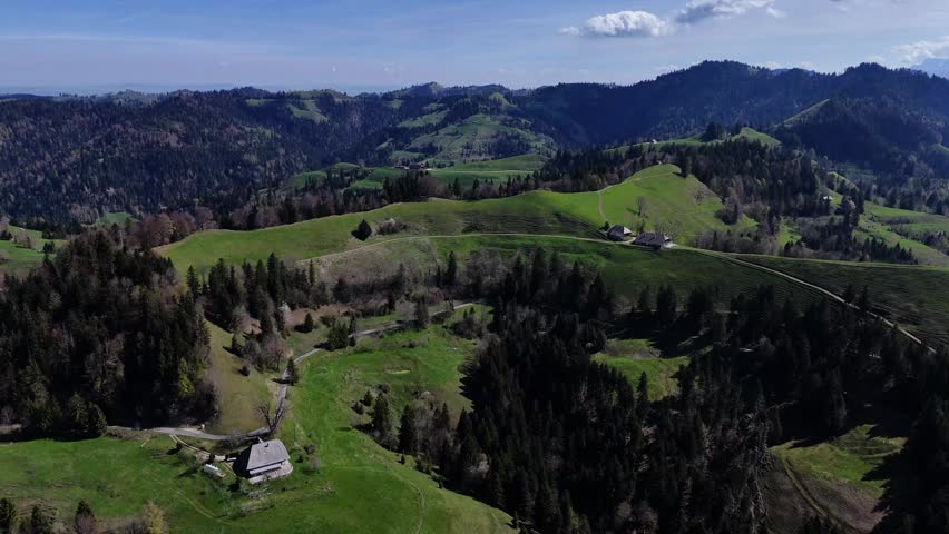 Wide landscape of rolling green hills, forests, and distant mountains under a clear blue sky in Emmental, Switzerland.