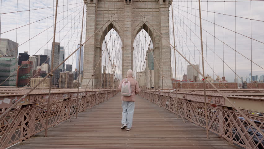 Young woman walking on Brooklyn Bridge with Manhattan skyline in New York.