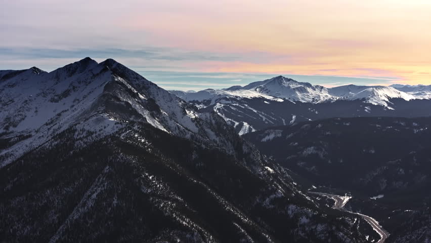 A cinematic, high-flying wide-angle aerial drone shot of snowy peaks surrounding Dillon and Frisco, slowly revealing the ski slopes of Breckenridge Ski Resort in Colorado