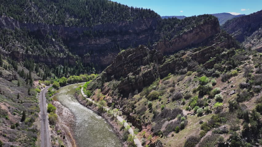 Cinematic wide-angle aerial drone shot reversing and rising above the Colorado River and I-70 through Glenwood Canyon, revealing dramatic Rocky Mountain terrain in Colorado.