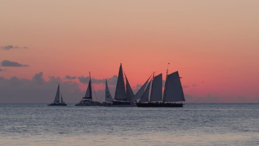 A stunning high-angle aerial view of Key West Harbor in the Florida Keys. The footage captures a diverse array of maritime vessels, from modern luxury motor yachts to classic sailboats, navigating or anchored in the shimmering turquoise and emerald waters. The shot highlights the bustling nautical lifestyle of the harbor, with the tropical shoreline and historic Key West architecture in the background. Perfect for luxury lifestyle content, maritime documentaries, and Florida tourism videos focusing on high-end travel and sailing adventures.