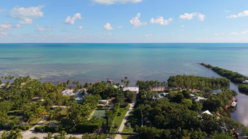 A cinematic high-angle aerial view of a road trip journey along the Seven Mile Bridge, part of the legendary Overseas Highway. The footage follows the flow of traffic as it travels over the vast, shimmering turquoise waters that separate the Middle and Lower Keys. Parallel to the modern highway, the historic old railway bridge adds a touch of heritage to the tropical landscape. This expansive establishing shot is perfect for travel vlogs, automotive commercials, and tourism campaigns showcasing the adventure of driving through the Florida Keys archipelago.