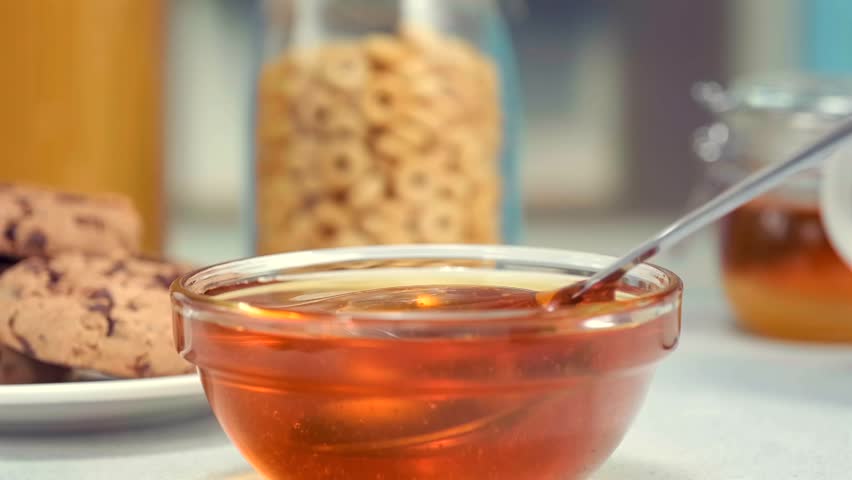 Honey dripping from spoon into glass bowl macro food texture dessert syrup copy space