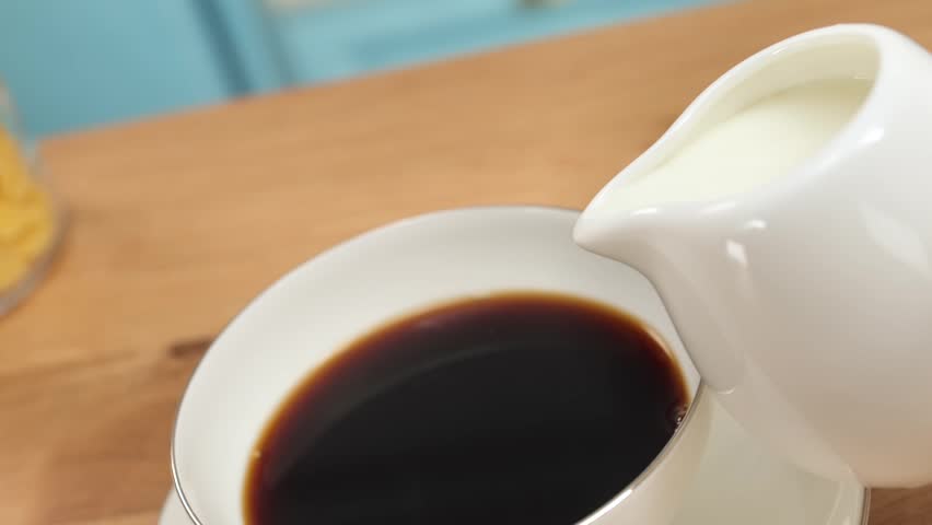 Cream pouring into hot coffee in glass cup creating smooth swirl, copy space