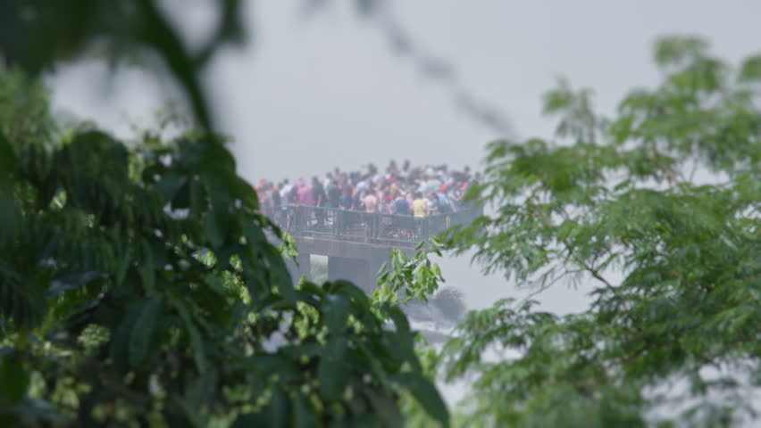 Crowd of people watch powerful Iguazu waterfall with strong water flow from the dedicated platform