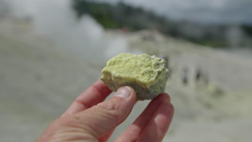 Piece of soil with sulfur. Person holds and rotates the yellow volcanic rock rich of sulfur. Volcanic active area of volcano of Mendeleev on Kunashir Island, Russia