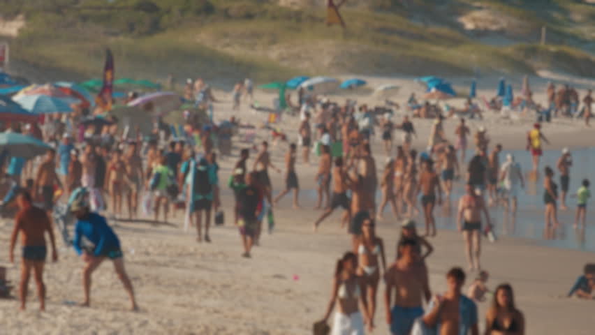 Crowded Santinho beach with people walking near the water. Florianopolis, Brazil