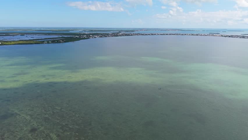 A stunning high-angle aerial view capturing the natural beauty of the Florida Keys seascape. The footage focuses on the vast expanse of shimmering turquoise and deep blue waters surrounding the Seven Mile Bridge area. The clarity of the ocean reveals the sandy textures of the seafloor below, illustrating the pristine marine environment of the Florida Keys National Marine Sanctuary. This tranquil and scenic water background is perfect for luxury travel documentaries, nature films, and tropical-themed commercial projects.