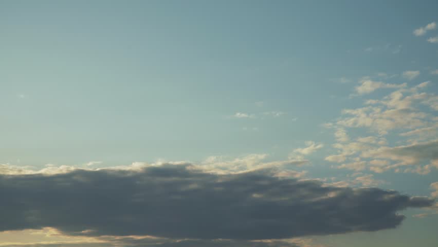 A bird glides across a sky with contrasting light and dark cloud layers on a blue sky. Soft sunlight illuminates the scene, highlighting the avian silhouette during a smooth panning motion view.