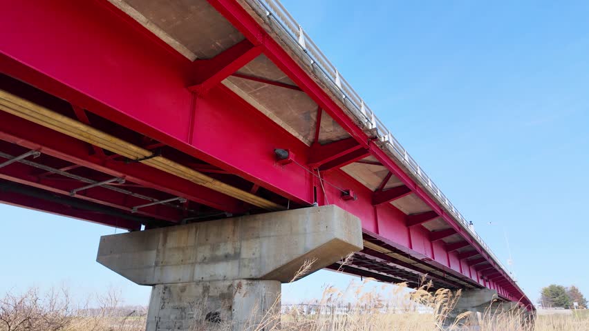 Looking up at a red bridge spanning a river in the tohoku region of Japan under a blue sky