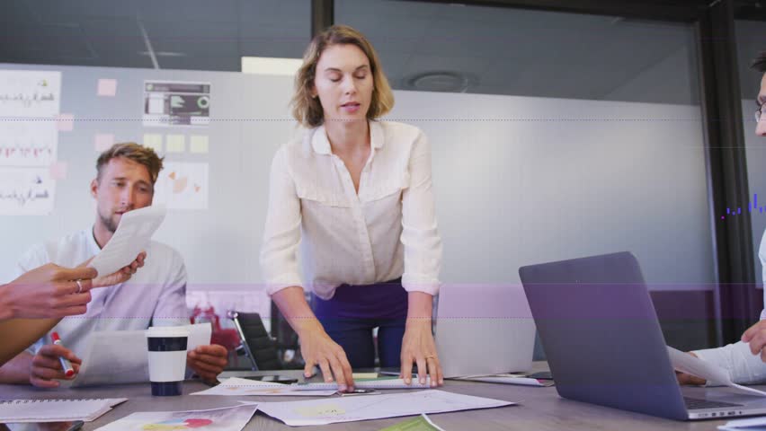 Leading mid adult woman distributing charts at conference table, in light blouse and dark trousers. Collaboration, meeting, documents, dashboard, data, analytics, boardroom