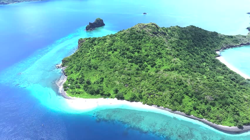 An aerial view captures the lush green landscape of a tropical island surrounded by blue water.
