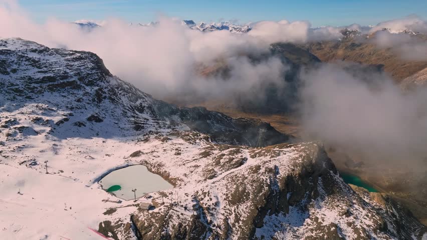 Aerial view of a secluded mountain lake surrounded by snow capped peaks and thick rolling clouds