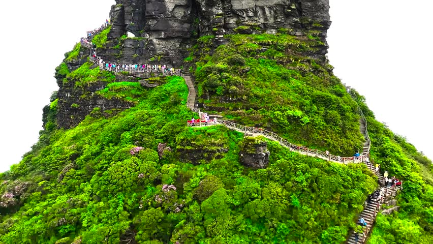 A scenic view of a lush green mountain path winding up towards a rocky summit in rural landscape