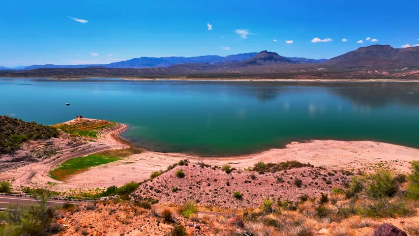 A serene landscape view of a calm blue lake surrounded by dry hills under a bright sunny sky