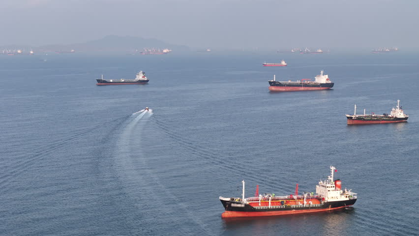 fast patrol boat in the foreground. Global energy transport with LPG gas and oil tanker ships anchored in the ocean, war energy crisis, and Strait of Hormuz blockade concept.