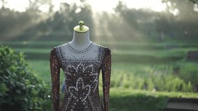 An exquisite, intricately beaded and embroidered formal gown displayed on a mannequin outdoors amidst a beautiful green landscape. Soft golden light enhances its luxurious details. - Powered by Shutterstock - Get 15% off with code: PIKWIZARD15
