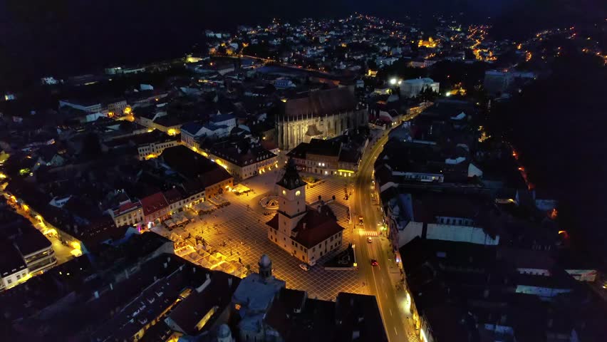 Aerial panorama of a vibrant city square at night with illuminated buildings and lively streets.
