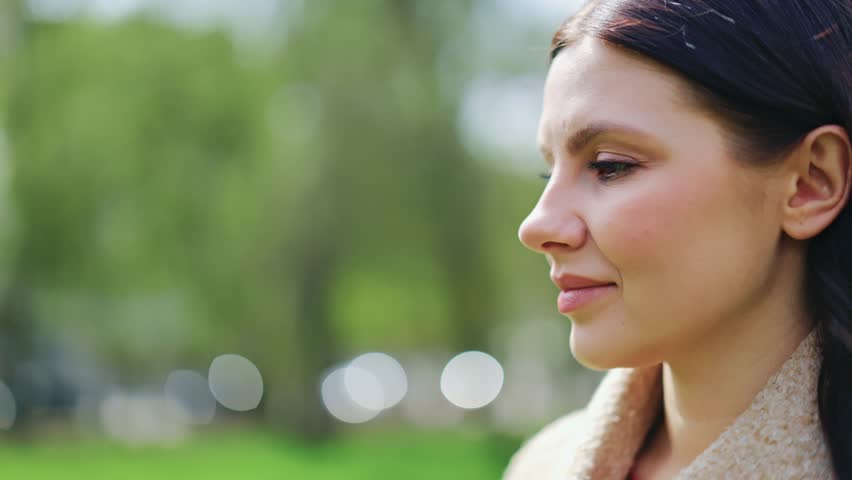 Beautiful woman with a peaceful, happy expression enjoys tranquil moment outdoors. Gentle sunlight illuminates face, conveying contentment and optimism amidst green nature. Thoughtful and serene mood is present.