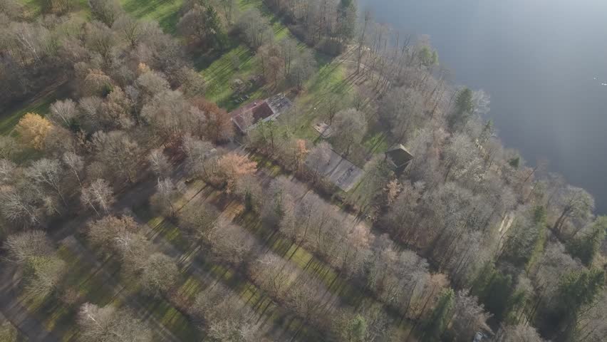 Aerial view of lakeshore with trees and scattered houses, calm natural landscape with water edge and rural buildings, peaceful atmosphere