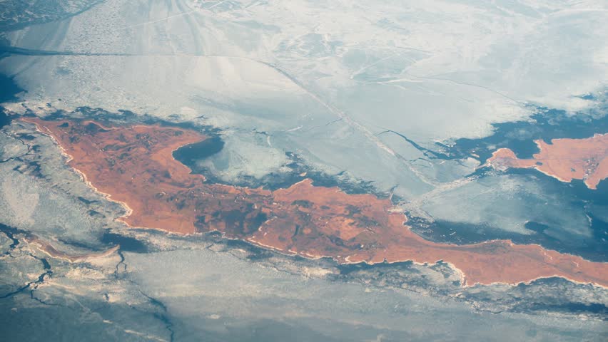 Aerial view while flying to Helsinki, Finland, showing frozen sea ice in Baltic, reddish shoreline islands, and striking winter textures along the Nordic coast.