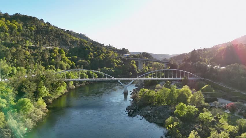 Majestic aerial view of a river valley with lush forests, a pedestrian bridge, and a highway