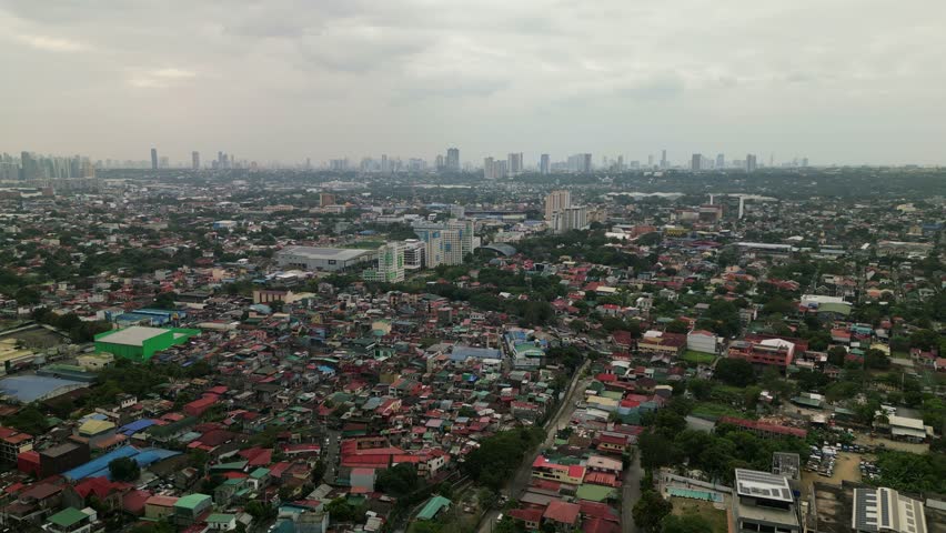 Aerial flyover shot of Antipolo, Philippines showcasing dense residential areas with distant skyscrapers under a cloudy sky.