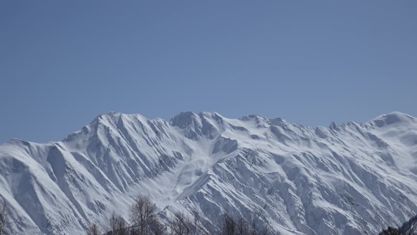 Handheld zoom shot of high snow-covered mountain peaks under clear sky. Slight camera shake adds a real immersive feeling of being in the mountains, natural travel atmosphere