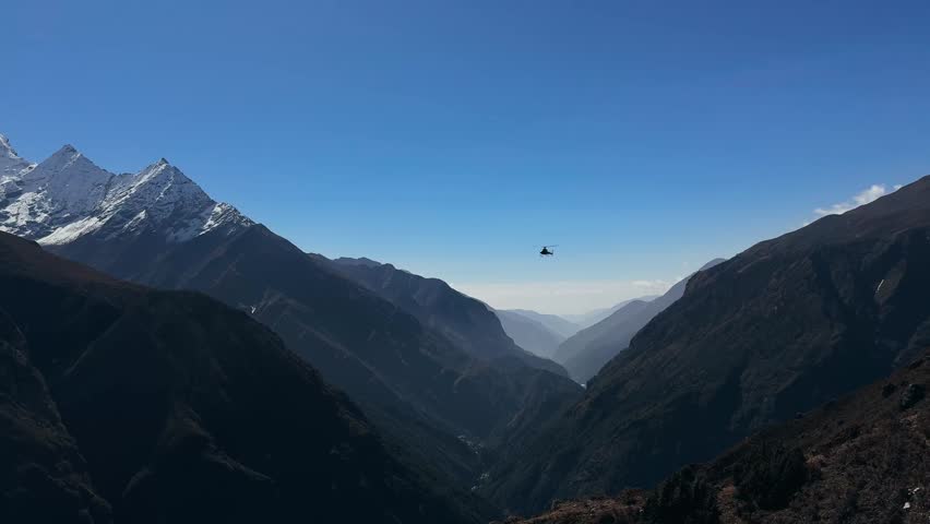 Helicopter flying over high Himalayan mountain peaks along the Everest Base Camp trekking route in Nepal. Aerial view of dramatic landscapes, snow-covered summits and deep valleys, adventure travel and extreme destination concept