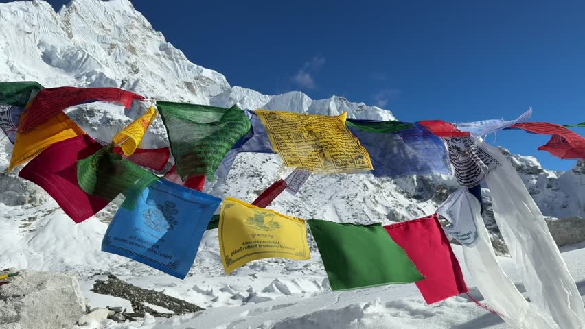 Tibetan prayer flags waving in wind near Everest Base Camp, Nepal. Snowy Himalayan mountains and blue sky. Spiritual travel concept. Slow motion video